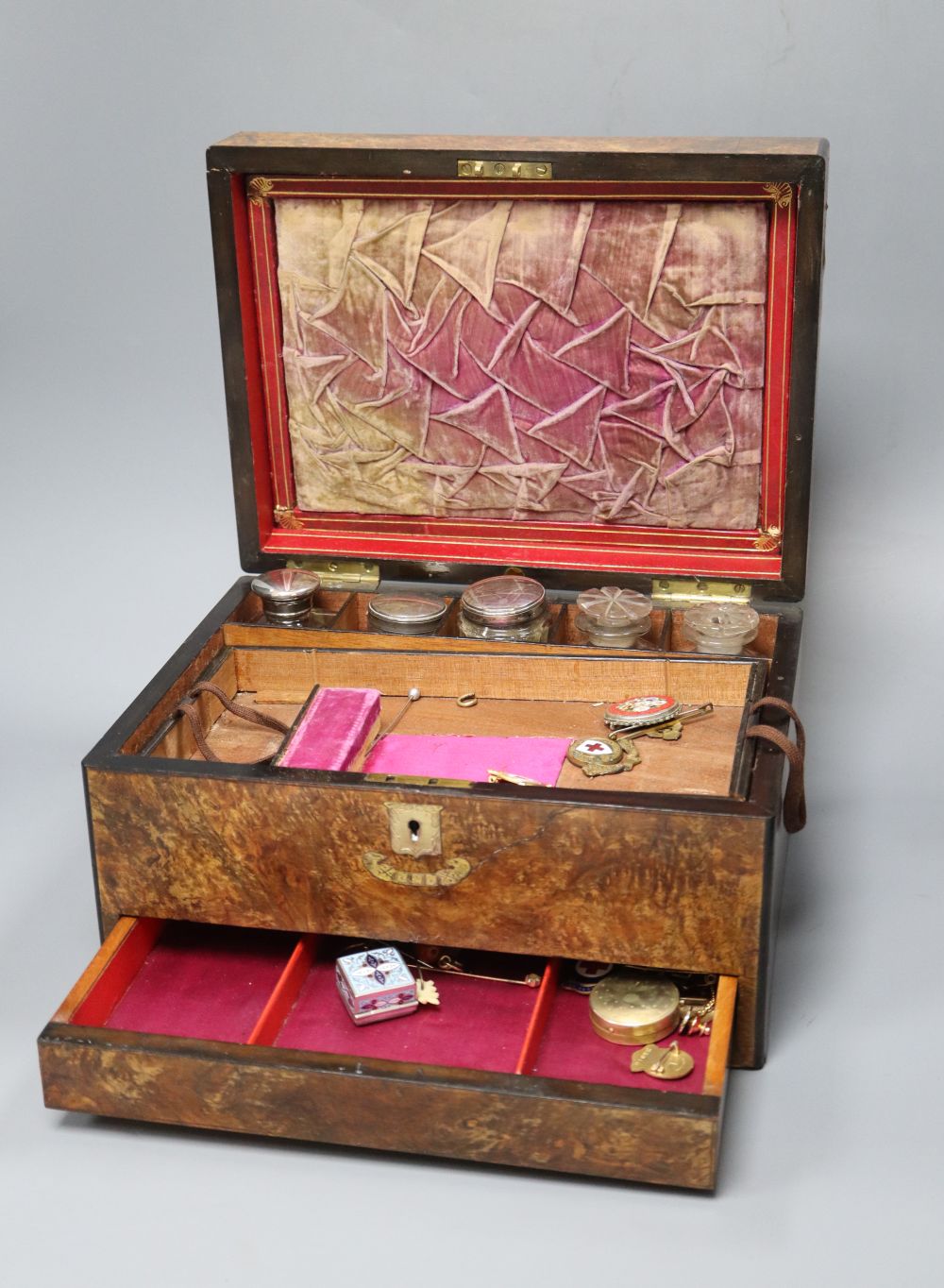 A walnut toilet box, containing four bottles and assorted badges and jewellery etc.